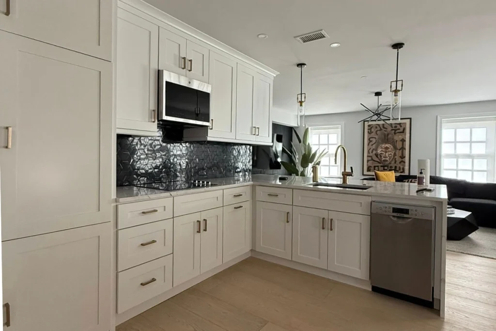 Contemporary Kitchen Remodeling in Glassboro NJ with white shaker cabinets, black tile backsplash, stainless steel microwave, dishwasher, and gold faucet accents creating a modern open-concept design