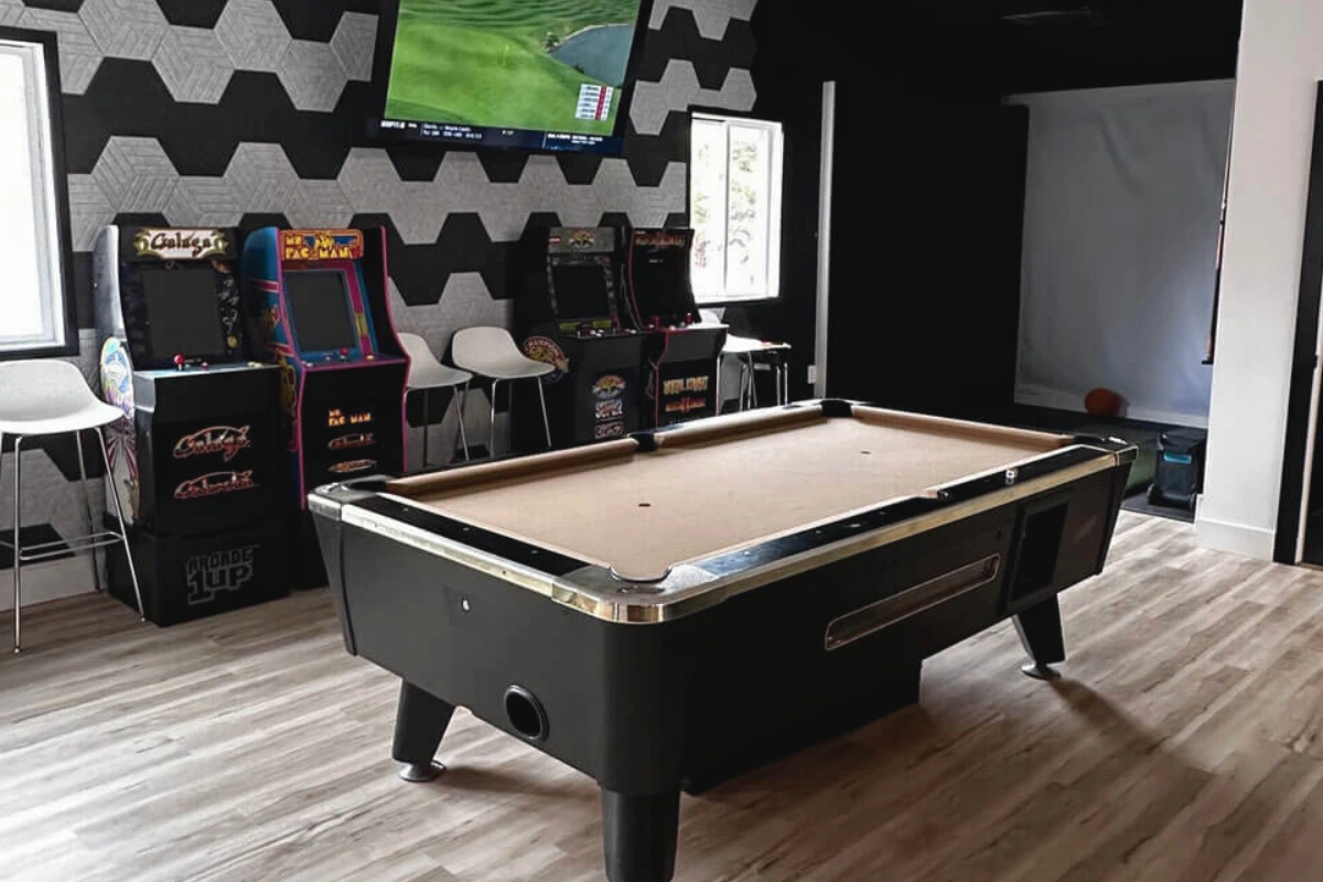 Modern custom home builds game room in washington township nj featuring a pool table, arcade machines, and stylish geometric wall design.