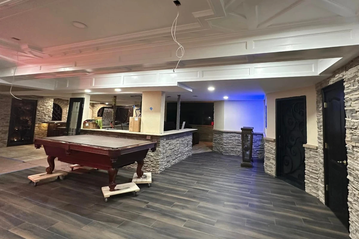 Luxury basement finishing project in Washington Township NJ featuring stone accent walls, dark wood-look flooring, recessed lighting, and a pool table area with a custom coffered ceiling design.