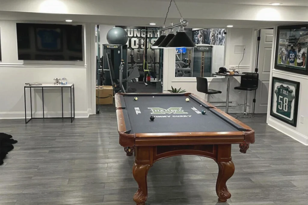 Modern basement finishing in Washington Township NJ featuring a sports-themed wall decor, and a connected home gym area for a functional and contemporary entertainment space.