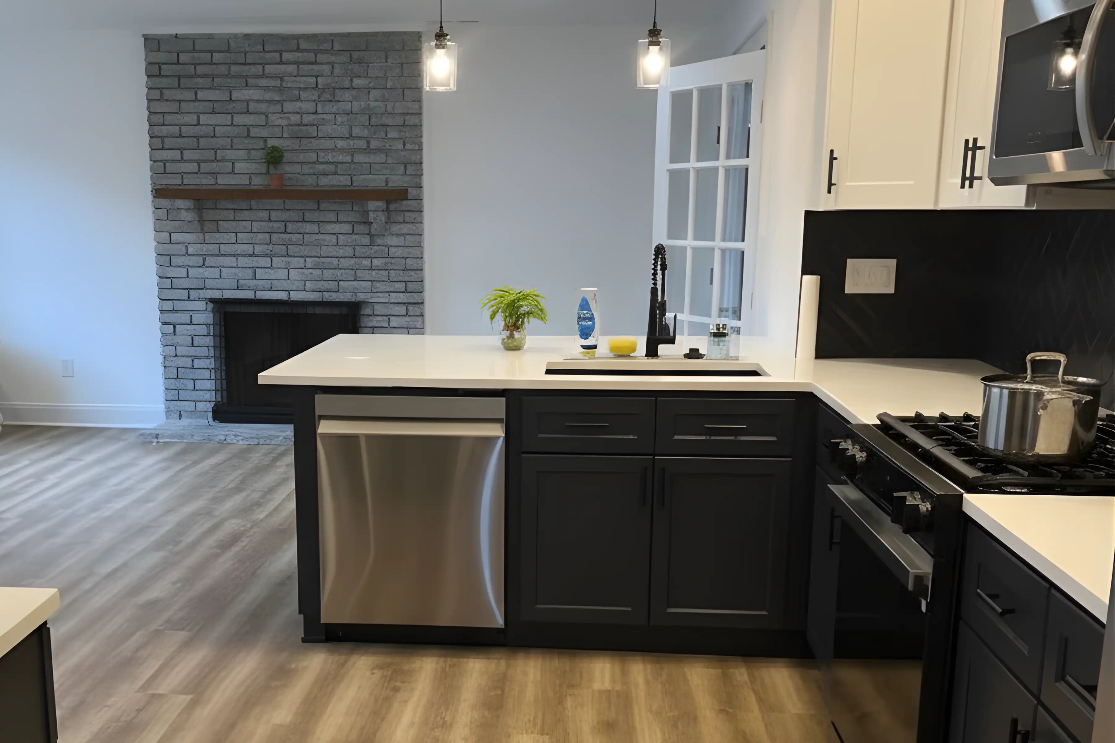 Modern open-concept kitchen remodel in Turnersville, NJ, featuring dark charcoal lower cabinets, white quartz countertops, a stainless steel dishwasher, and a grey brick fireplace in the background.