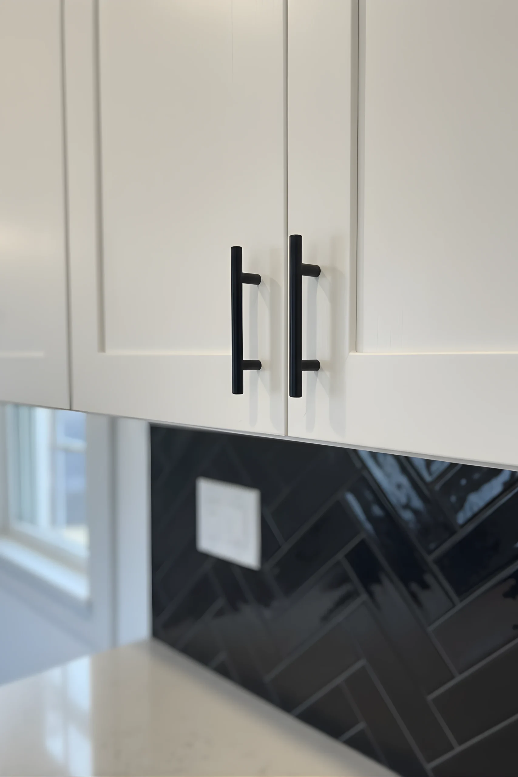 High-contrast Turnersville kitchen remodel showcasing a striking black glass herringbone backsplash against crisp white shaker cabinetry and industrial matte black hardware.