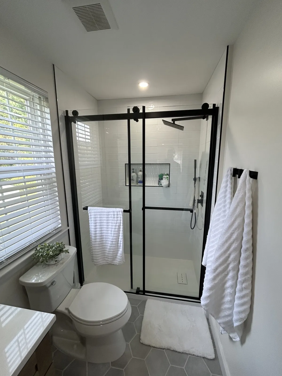 Full bathroom renovation in Philadelphia with black-framed glass shower enclosure, white subway tile, and hexagon floor tile