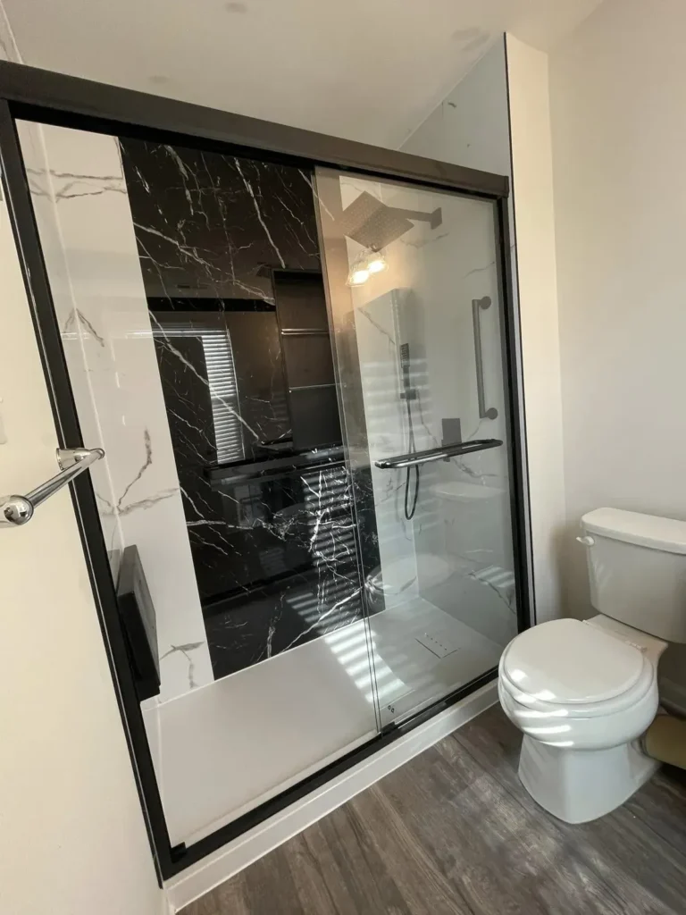 Bathroom with wood-look vinyl plank flooring and a black marble shower behind a black-framed glass door