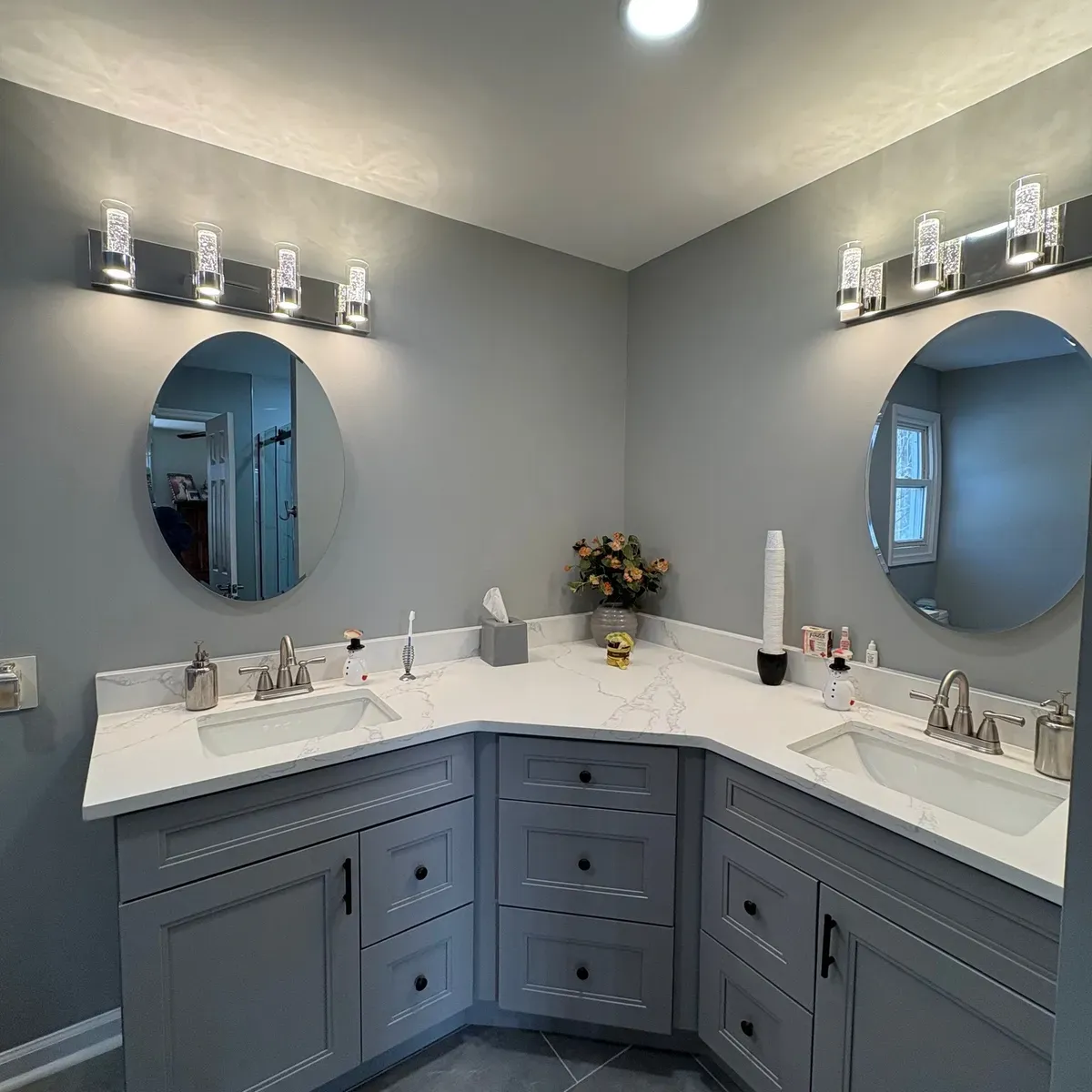 Updated bathroom with a gray corner double vanity, quartz top and two round mirrors