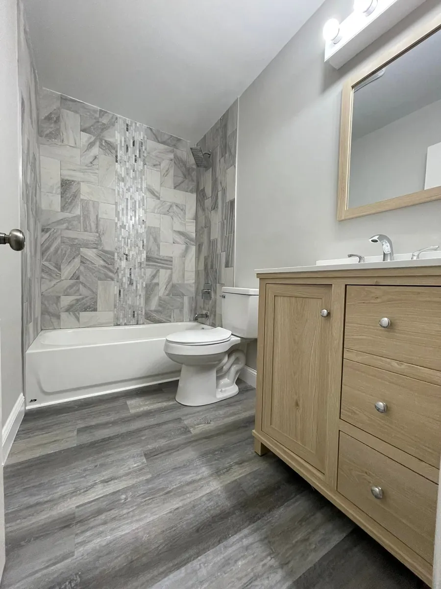 Tub shower with a marble-look accent wall and light wood vanity in Juniata Park, Philadelphia