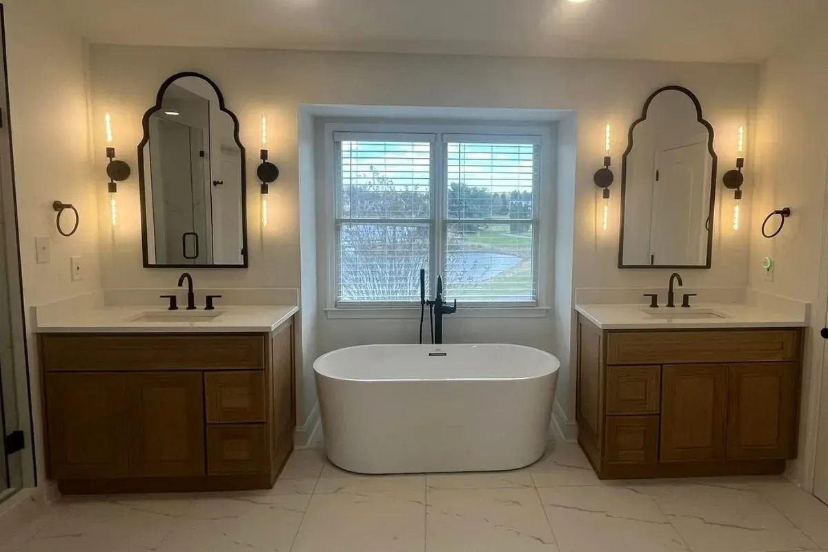 Arched mirrors over twin vanities with a soaking tub between in Mantua, Philadelphia