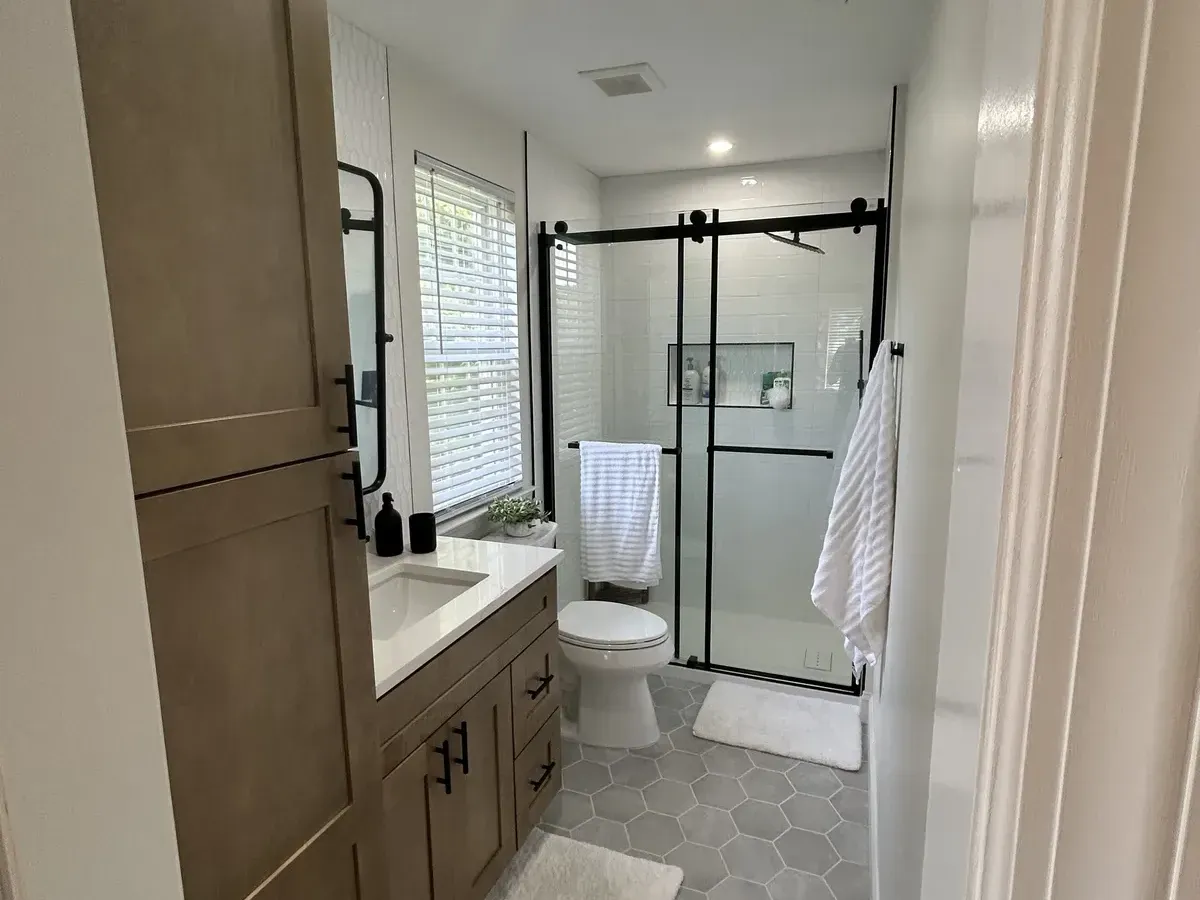 Wood vanity and tall linen cabinet with a black-frame shower in Spring Garden, Philadelphia