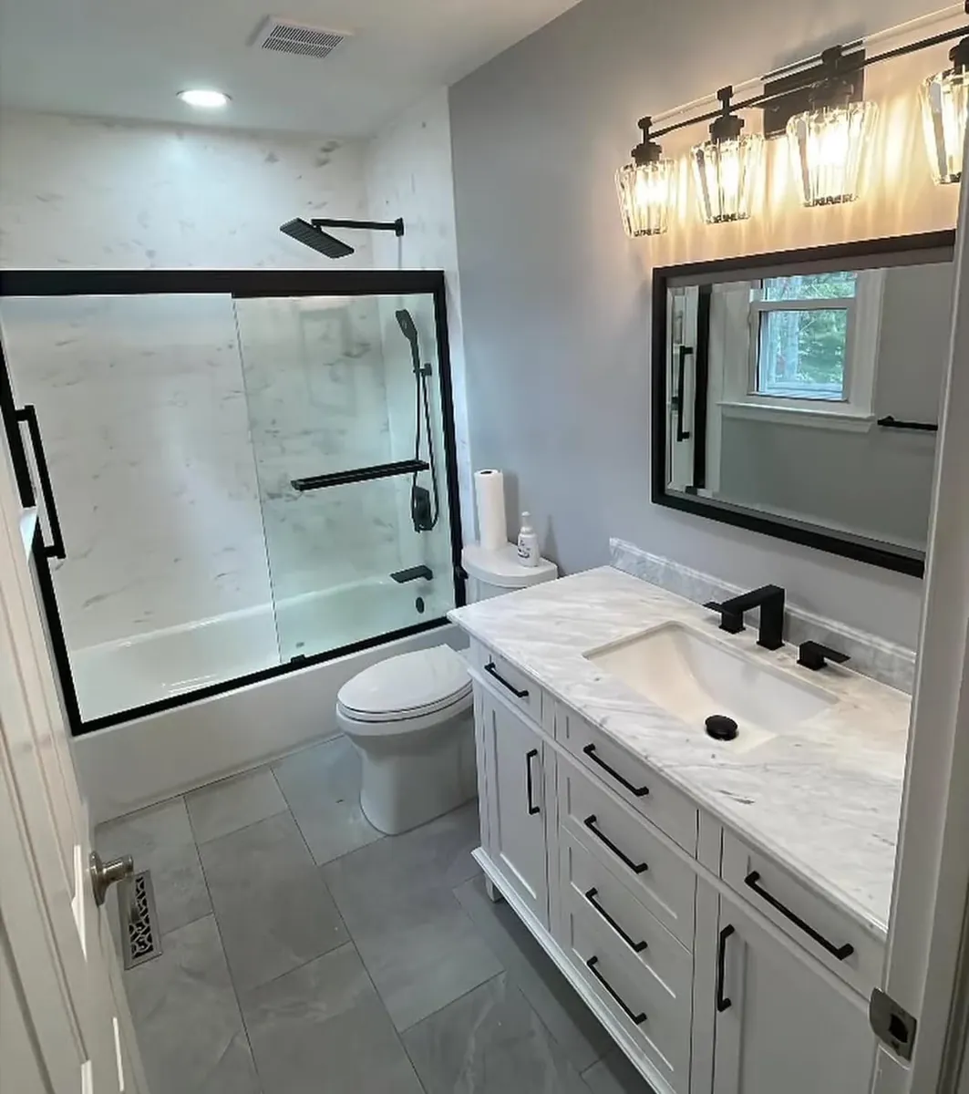 White vanity and marble-tile tub surround with a black sliding door in West Oak Lane, Philadelphia