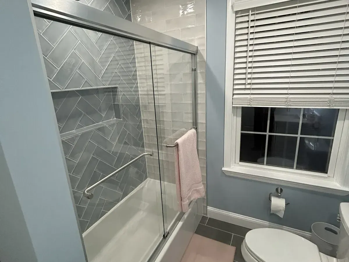 Herringbone tile tub shower next to a double-hung window in Wynnefield Heights, Philadelphia