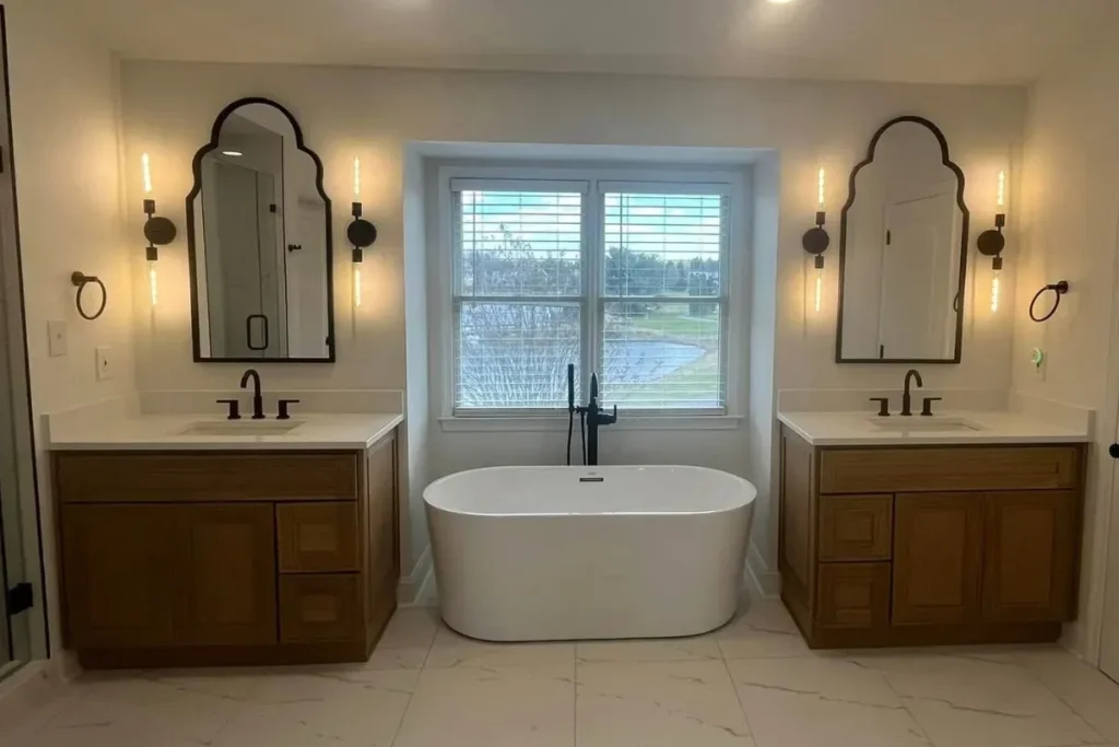 Freestanding soaking tub set between two wood vanities with arched mirrors after a bathtub replacement