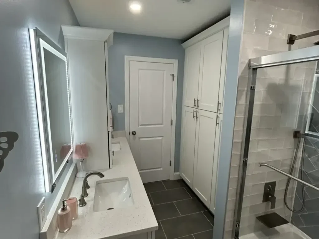 Bathroom with dark large-format floor tile, a lighted mirror and a glass shower enclosure