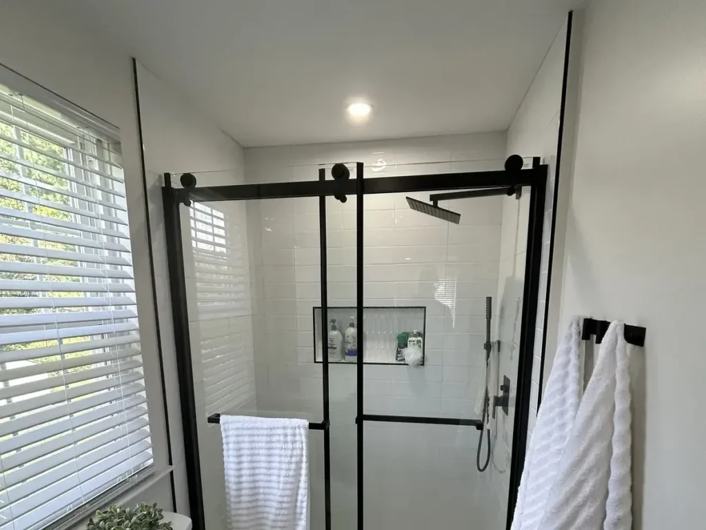 Shower retiled in white subway tile behind a black-framed sliding glass door