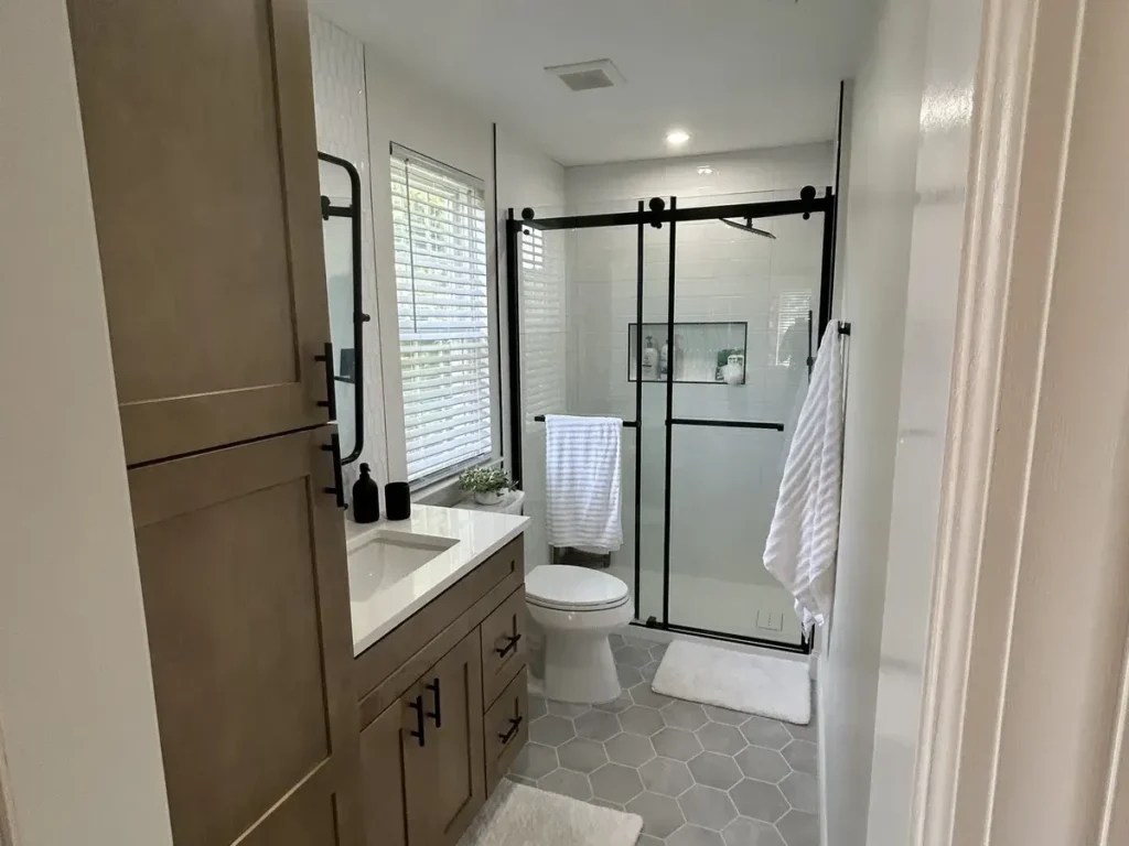 Narrow small bathroom remodel with a wood linen tower, single vanity and black-framed glass shower