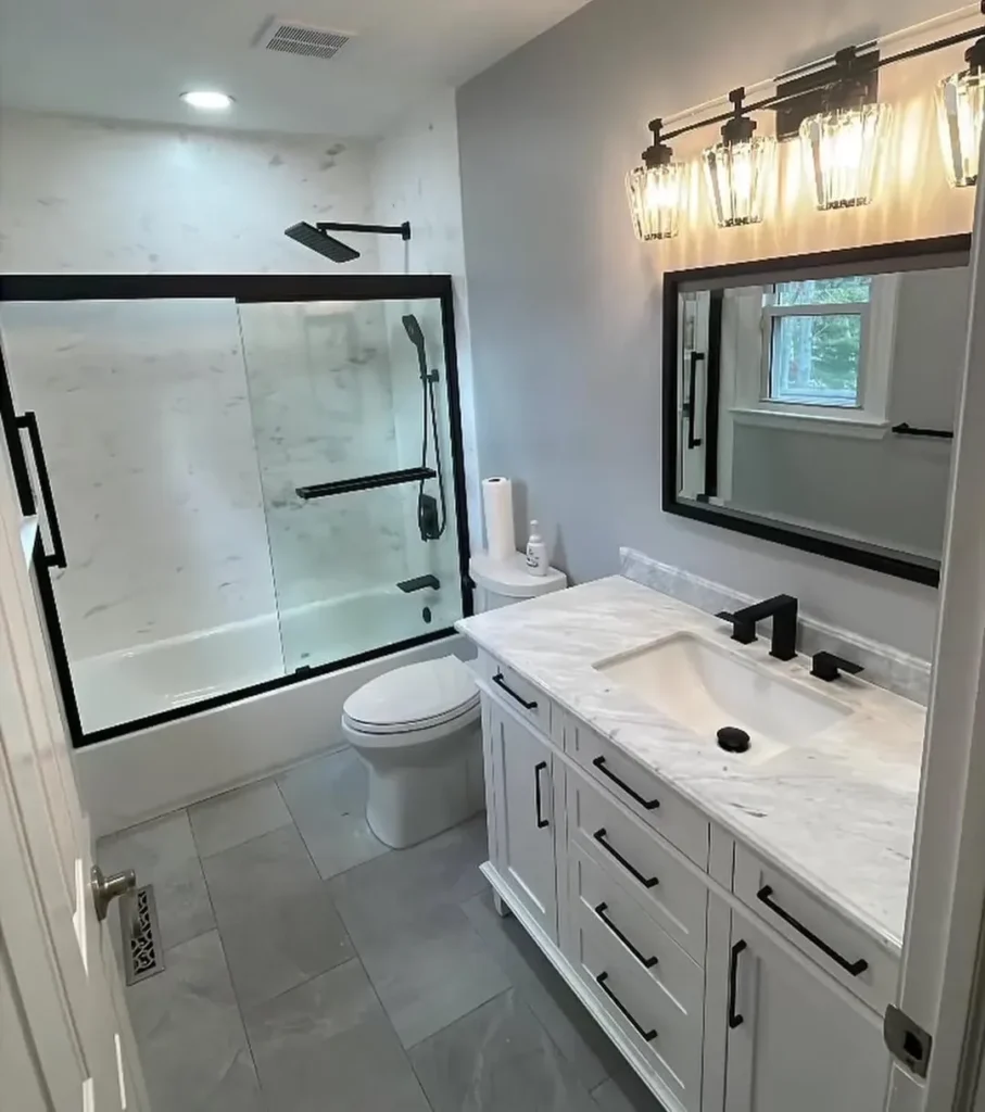 White vanity with a marble look top and backsplash, black framed mirror, and a four-light vanity fixture