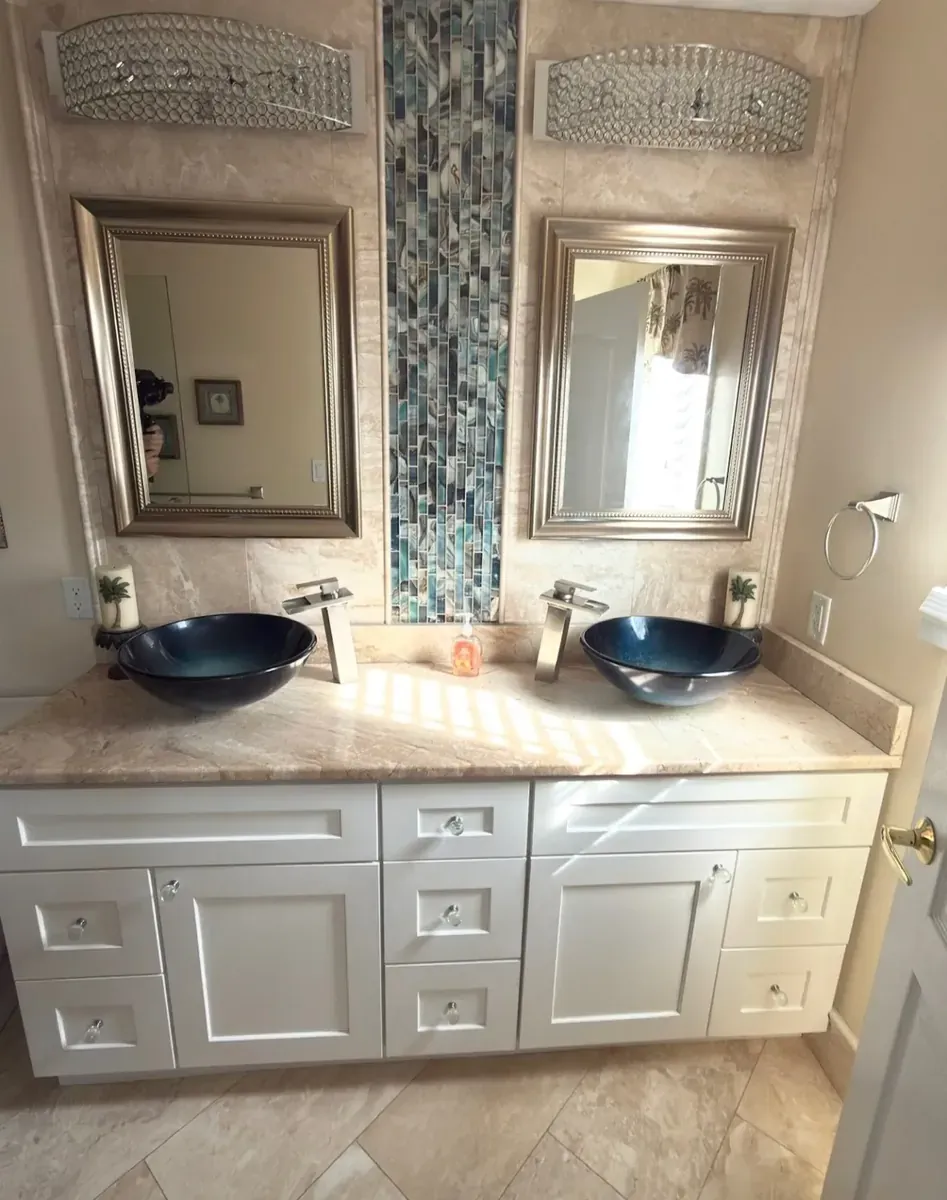 Double vanity with blue glass vessel sinks, stone backsplash, and a glass mosaic tile strip between two mirrors