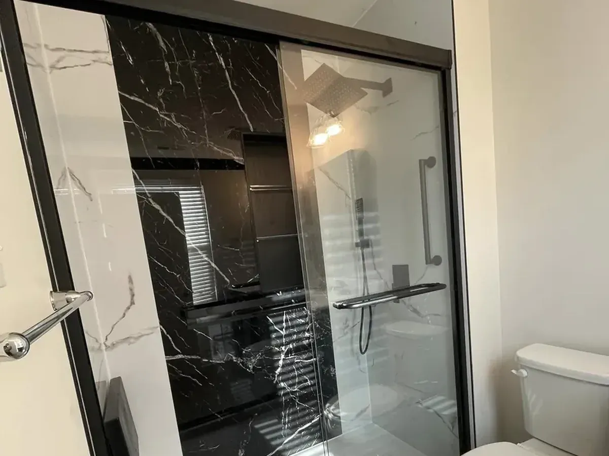Rebuilt bathroom after demolition with a black marble look shower, sliding glass doors, and a new toilet