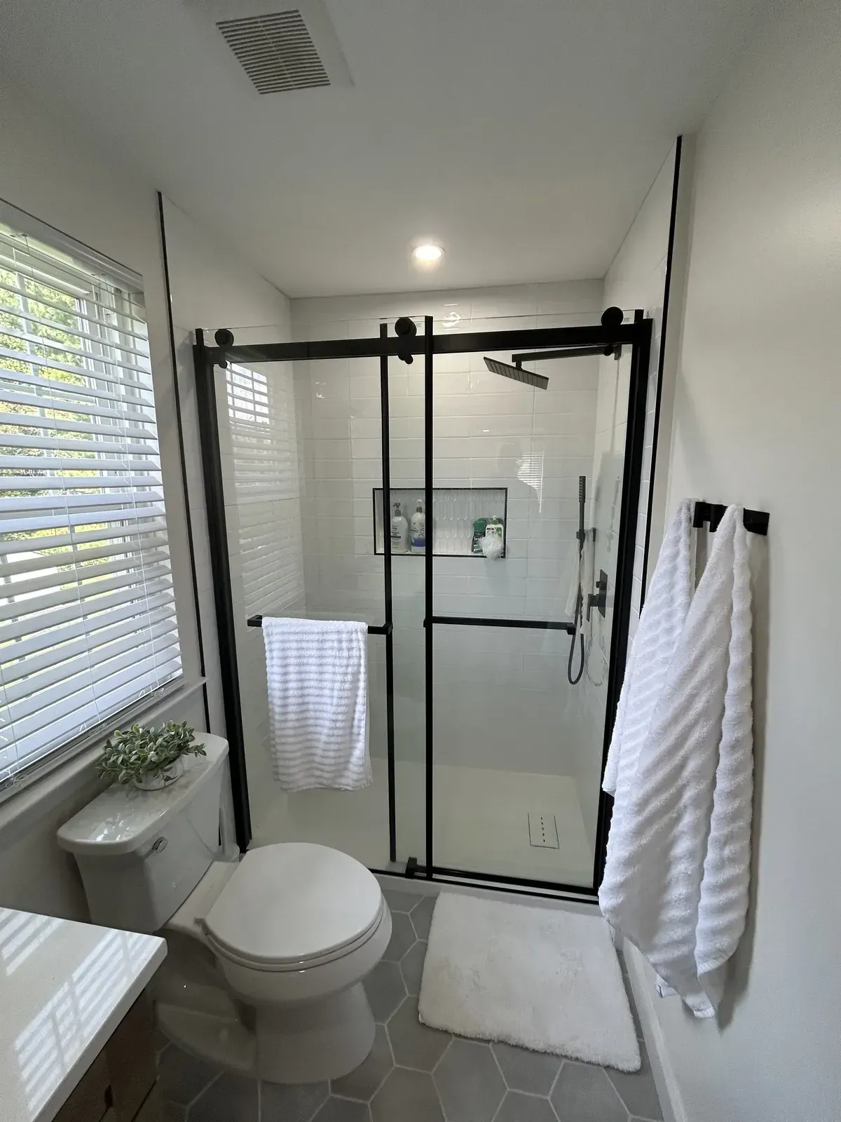 Bathroom ceiling exhaust fan above a black framed sliding shower with white subway tile and a window