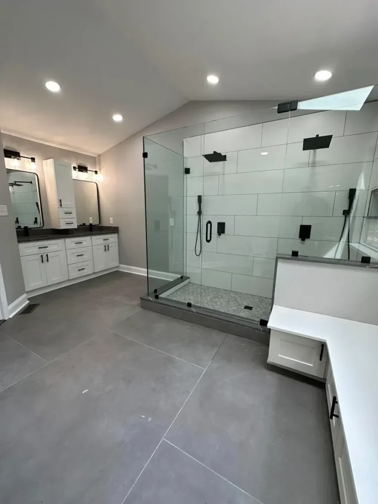 Reconfigured open bathroom layout with a large frameless glass shower, a bench, and a white vanity across the room