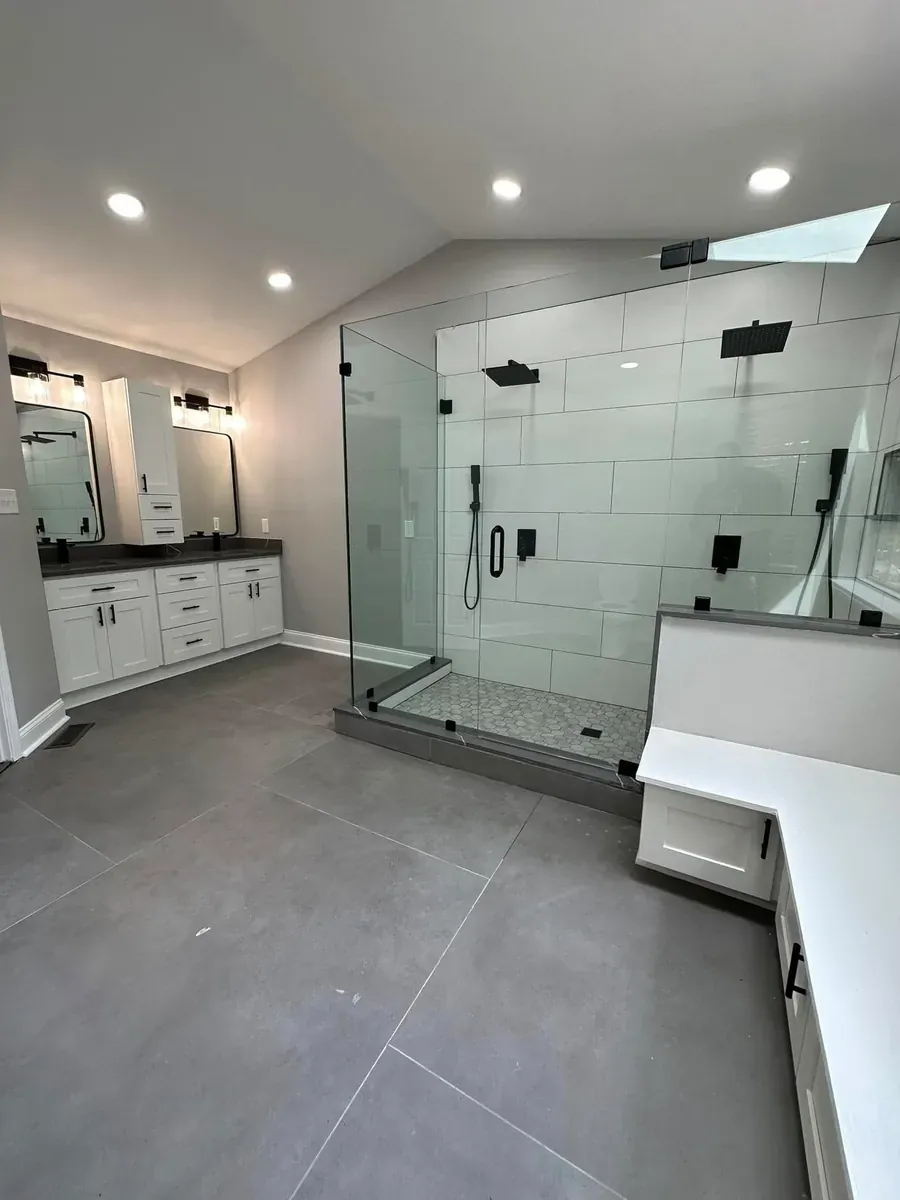 Reconfigured open bathroom layout with a large frameless glass shower, a bench, and a white vanity across the room
