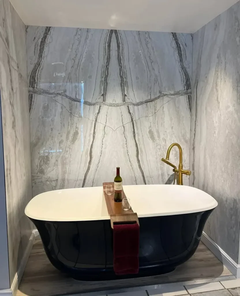 Black freestanding tub with a gold floor-mount faucet against a marble slab wall