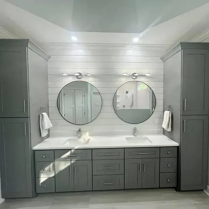 Remodeled bathroom with a gray double vanity, tall linen cabinets, round mirrors, and a shiplap wall