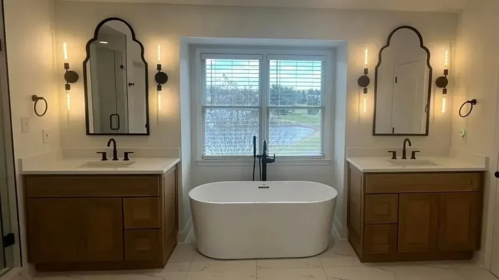 Twin wood vanities with arched mirrors framing a freestanding soaking tub under a window