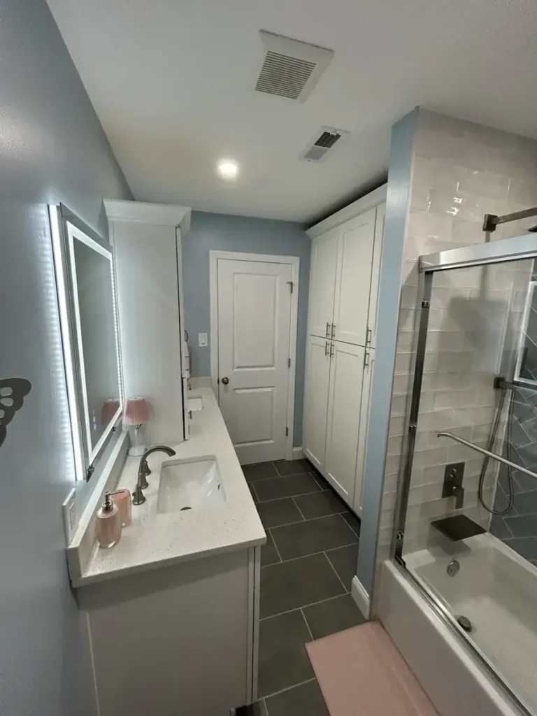 Remodeled bathroom with a ceiling exhaust fan, lighted mirror, white vanity, and a tub shower with glass doors