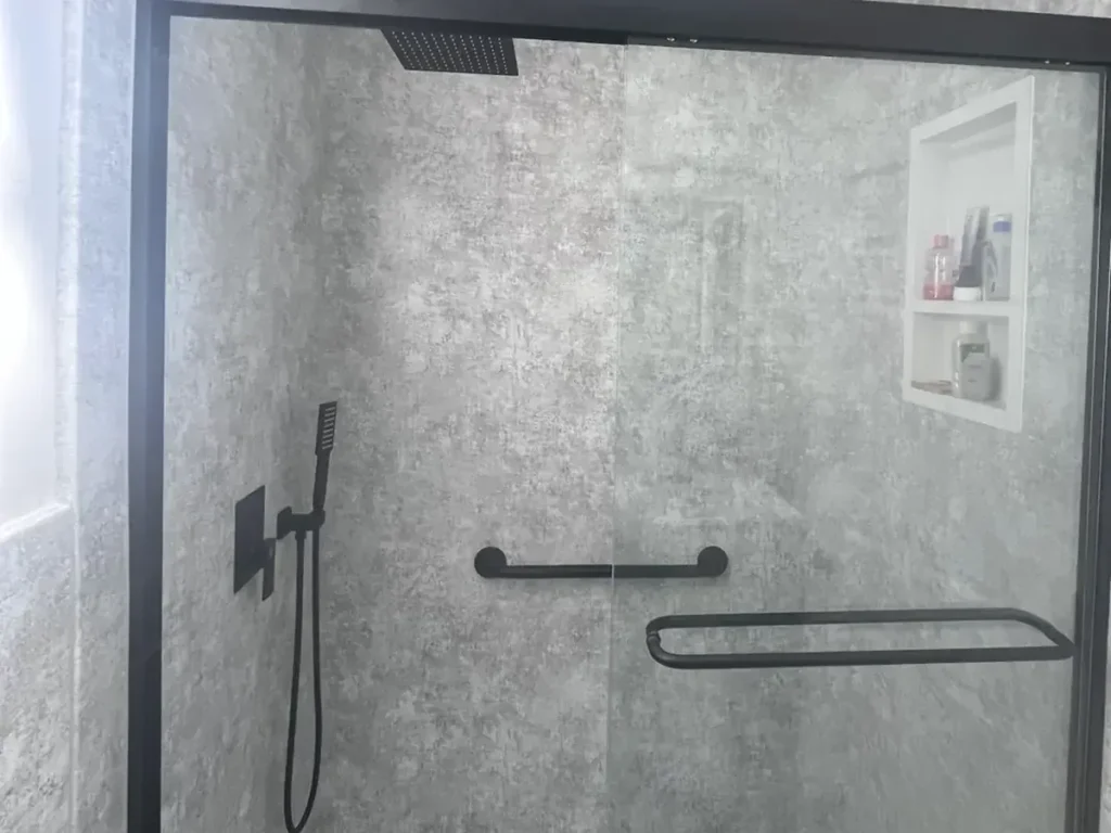 Waterproof gray stone look shower wall panels with a built-in niche, grab bar, and matte black fixtures