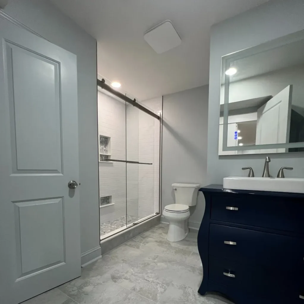 Bathroom with a navy vanity, white toilet and a subway tile shower with a glass door