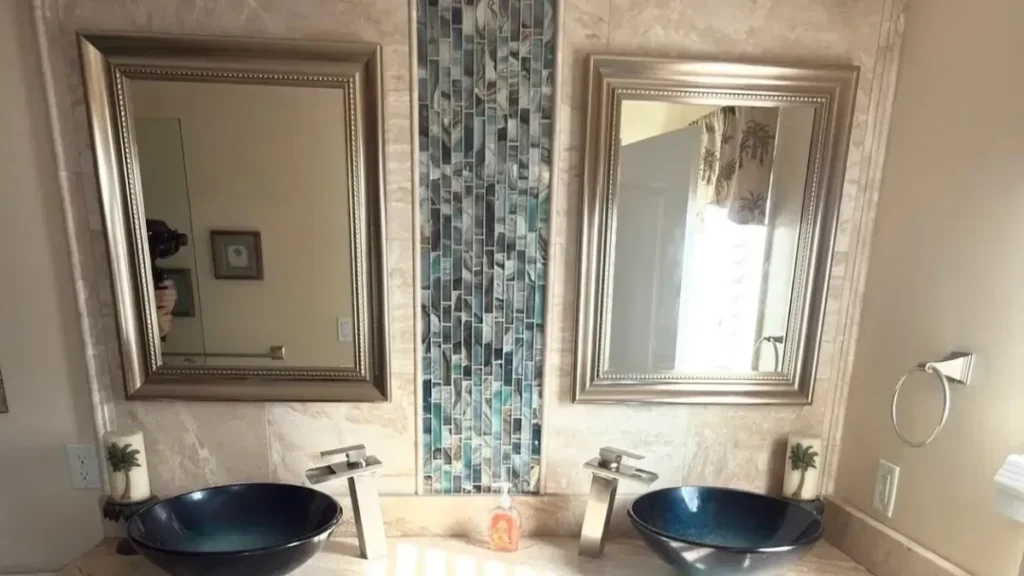 Glass mosaic tile accent strip between two mirrors above twin blue vessel sinks
