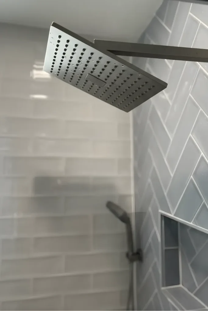 Square rain showerhead over white subway tile and a gray herringbone tile accent wall