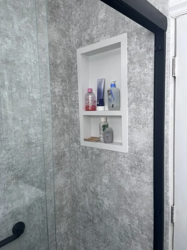 Recessed two shelf shower niche holding bottles in gray stone look shower wall panels