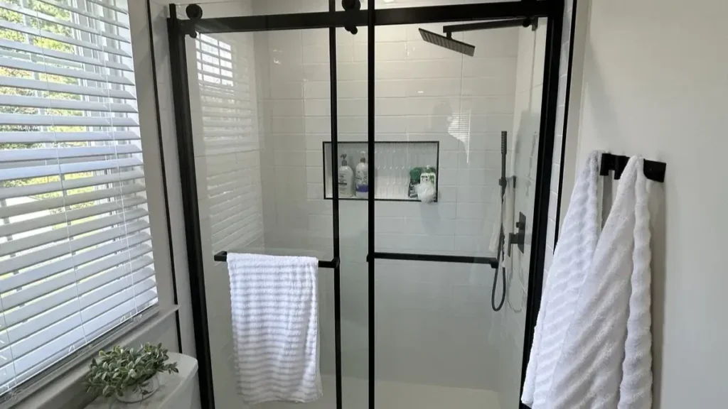 White subway tile shower with even grout lines, a tiled niche, and a black framed sliding glass door