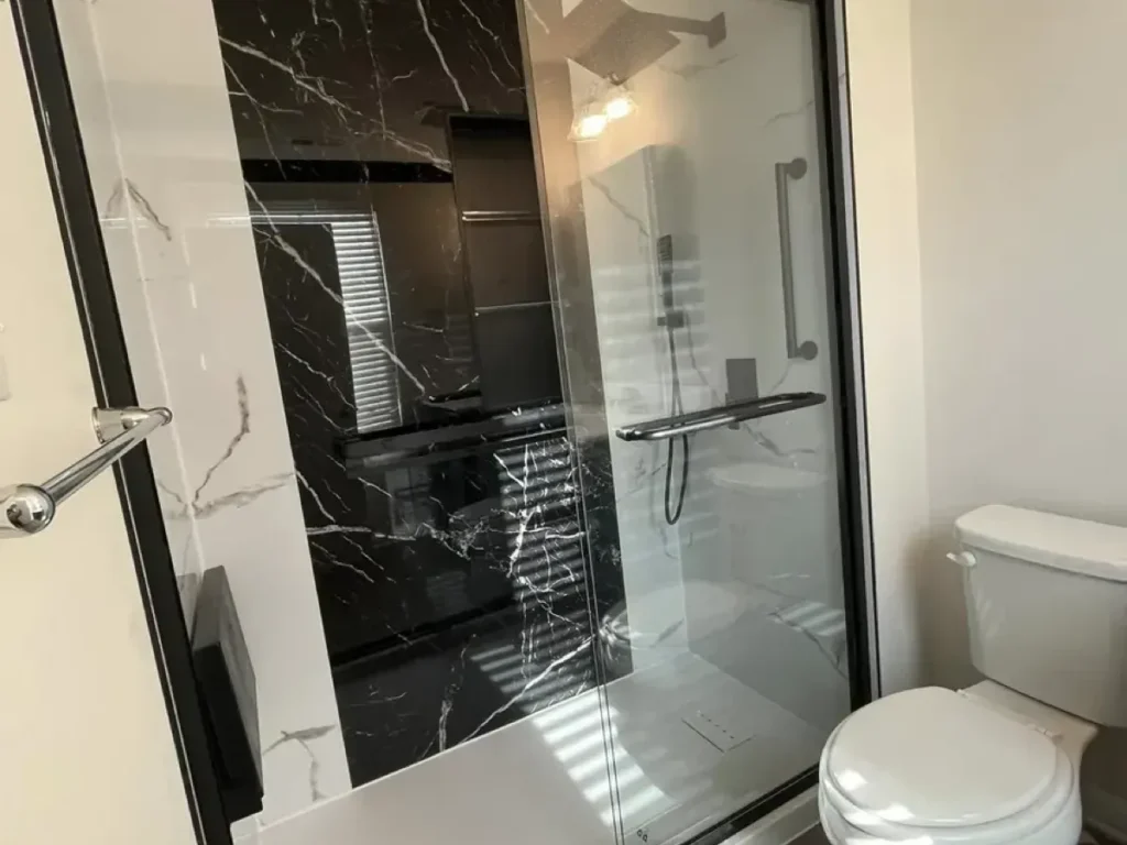 Glass shower enclosure with black marble-look walls and a chrome grab bar