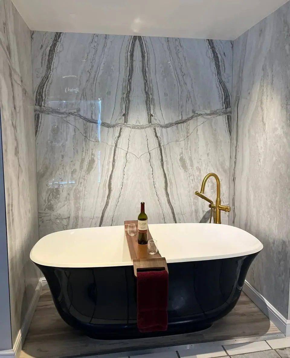 Black freestanding soaking tub with a gold floor-mounted filler in front of a gray veined stone look wall